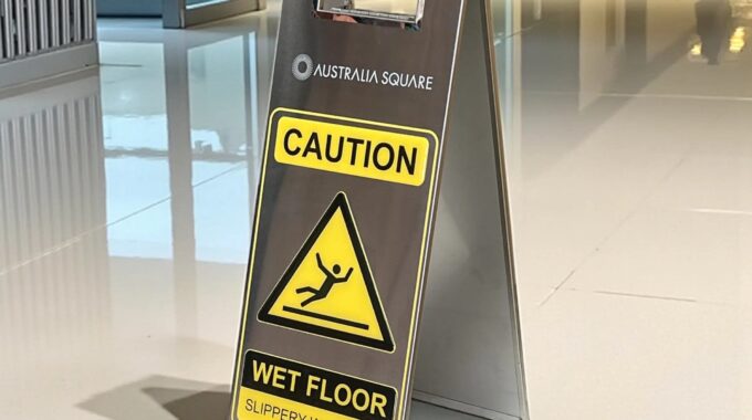 Stainless steel wet floor sign in silver, folding A-frame caution sign with yellow WET FLOOR panel, shown in a commercial building lobby
